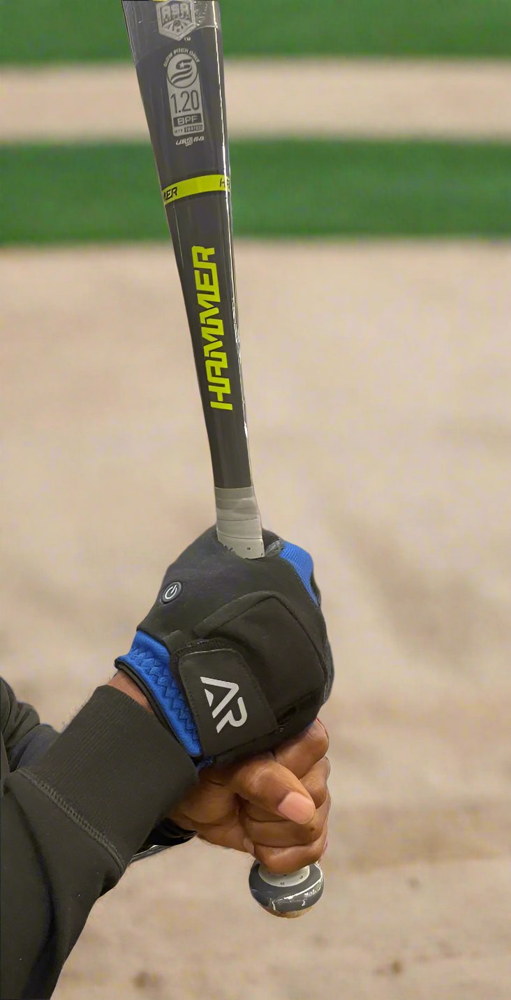 A person grips a Hanover baseball bat with an arcticreaction Black & Blue GEN2 Heated Sports Glove, preparing to swing. The image focuses on their hands and the bat, set against the blurred background of a baseball field, highlighting the glove's dual heat settings perfect for chilly days.
