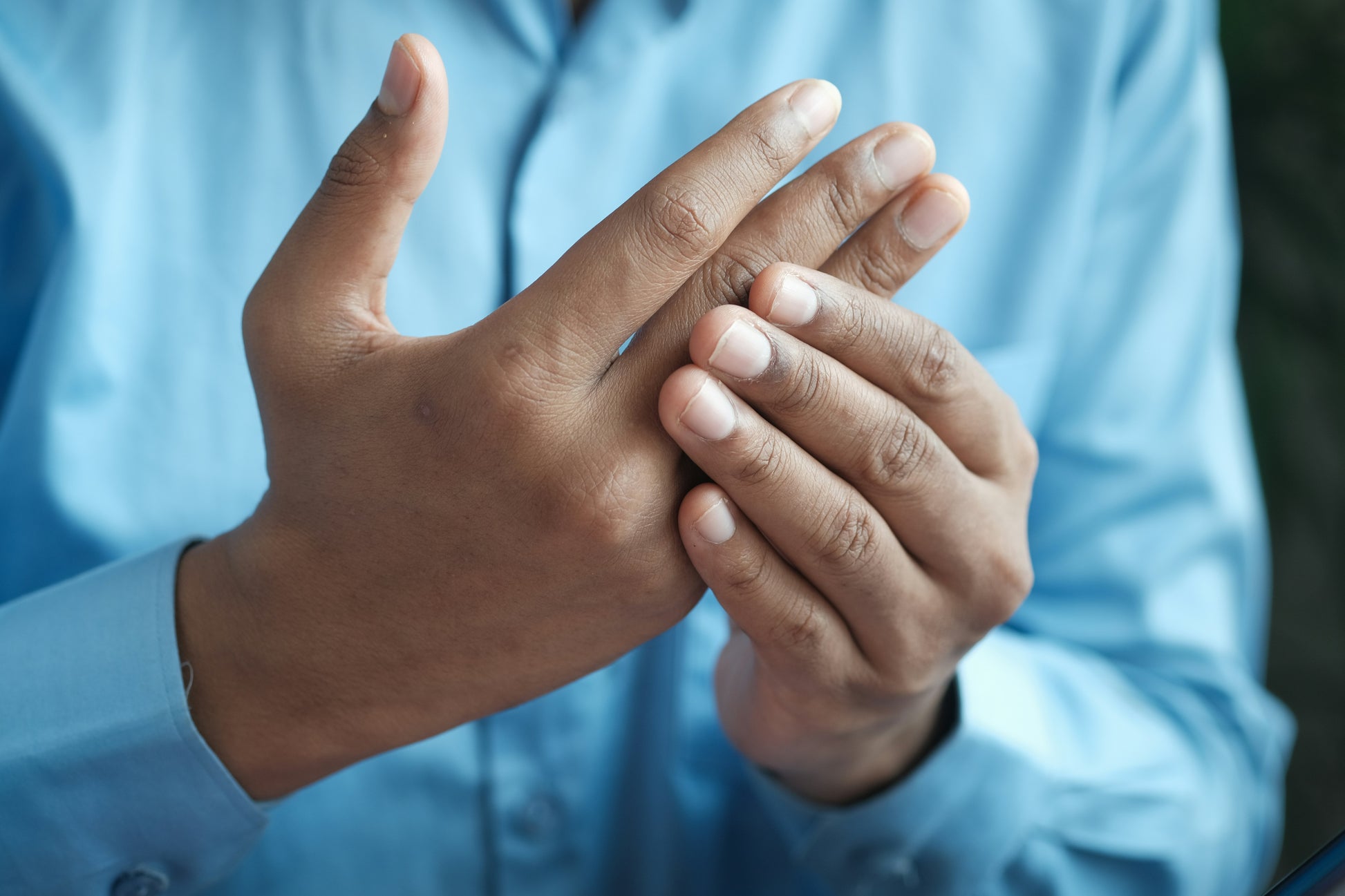 A person in a blue shirt is seen holding their left hand with their right, focusing on the fingers wrapped in the arcticreaction Black & Gray GEN2 Heated Sports Glove. The hands are shown close-up against a neutral background, emphasizing the glove's touchscreen compatibility.